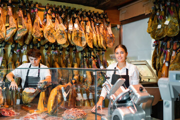Young couple work together in butcher shop - they cut the traditional Spanish jamon
