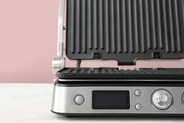Modern electric grill with open lid on white table against pink background