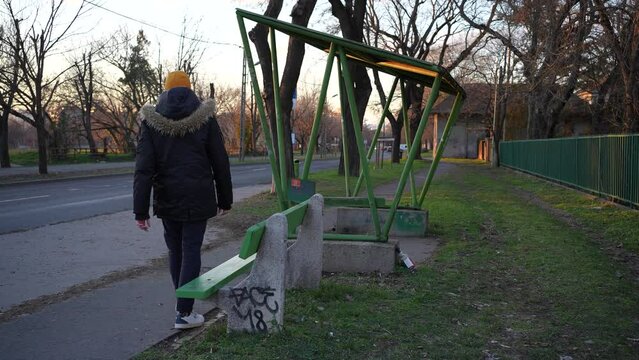 Sad depressed young man sitting down at a suburban bus stop