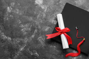 Diploma with red ribbon and graduation hat on dark grey table