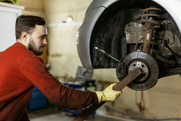 A hard-working mechanic with clothes stained with oil holds a homemade tool and unscrews a rusted...