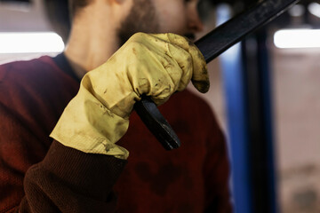 A hardworking mechanic with oil-stained clothing is working with a Crowbar underneath the bottom of...