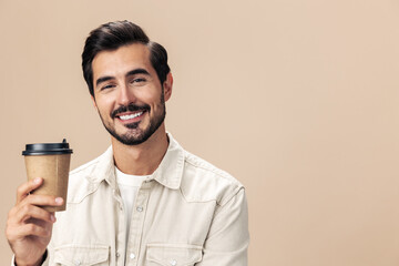 Portrait of a stylish man smile with a cup of coffee to go mock up on a beige background in a white t-shirt, fashionable clothing style, space space