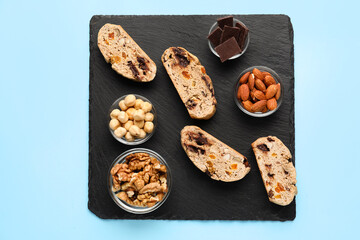 Slate board with delicious biscotti cookies, nuts and chocolate on blue background