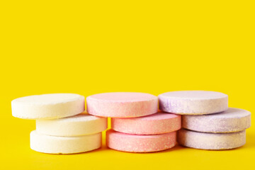Stacks of white, pink and lilac soluble tablets on yellow background