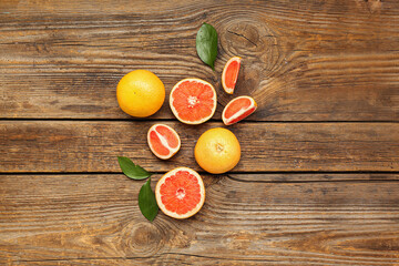 Composition with whole and cut grapefruits and plant leaves on wooden background