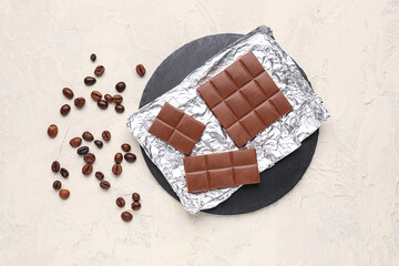 Board with pieces of tasty chocolate and coffee beans on light background