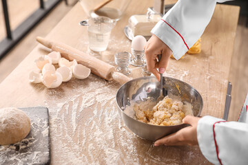 Female chef making dough for pasta at table in kitchen, closeup