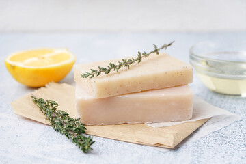 Stack of natural soap bars, lemon and thyme on light background