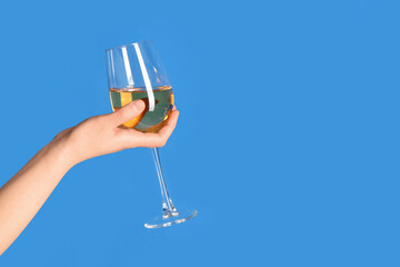 Female hand holding glass of white wine on blue background