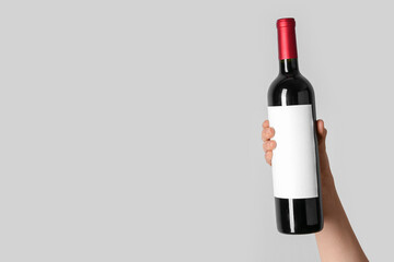 Female hand holding bottle of red wine on grey background