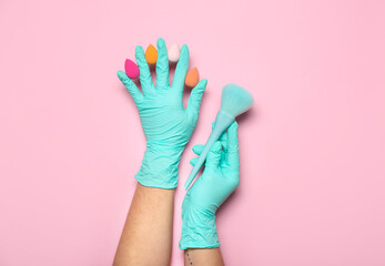 Makeup artist in rubber gloves with sponges and brush on pink background