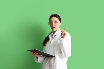 Female scientist with clipboard and raised index finger on green background