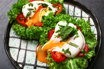 Plate with tasty eggs Benedict on black grunge table, closeup
