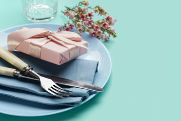 Table setting with gift box, cutlery and floral decor on turquoise background