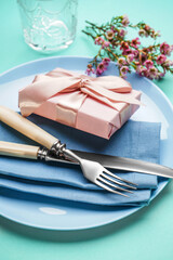 Table setting with gift box, cutlery and floral decor on turquoise background