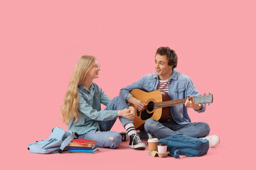 Teenage girl with her boyfriend playing guitar on pink background