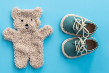 Baby shoes and bear toy on blue paper background. Newborn concept. Top view, flat lay