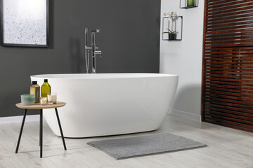 Obraz na płótnie Canvas Stylish bathroom interior with ceramic tub and care products on coffee table