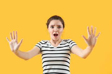 Scared young woman on yellow background