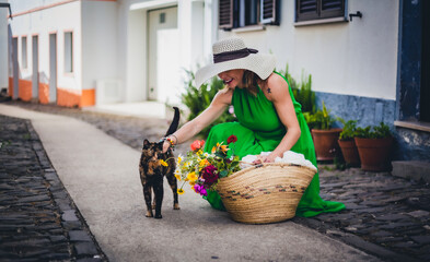 elegant woman in a old village street in the algarve hills with a basket of flowers cheering a cat