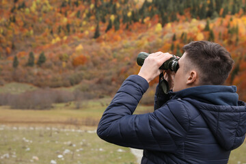 Boy looking through binoculars in beautiful mountains, back view. Space for text
