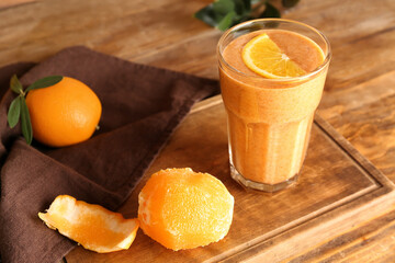 Board with glass of healthy smoothie and peeled orange on wooden table