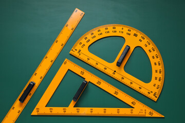 Protractor, triangle and ruler on green chalkboard, flat lay