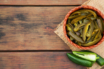 Fresh and pickled green jalapeno peppers on wooden table, flat lay