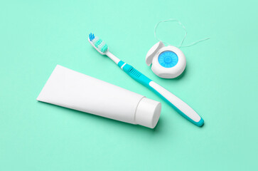 Dental floss, brush and tube of toothpaste on turquoise background
