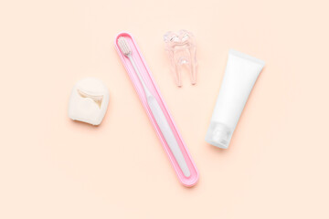 Dental floss, brush, plastic tooth model and tube of paste on beige background