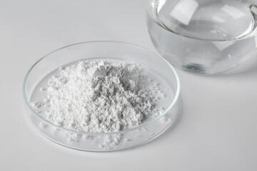 Fototapeta na wymiar Petri dish with calcium carbonate powder and laboratory flask on white table