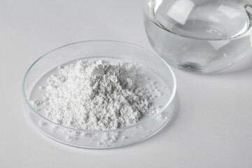 Petri dish with calcium carbonate powder and laboratory flask on white table