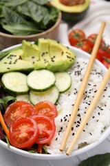 Delicious poke bowl with vegetables, avocado and mesclun on white table