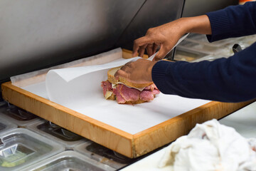 Hands of female diner employee wrapping deli meat sandwich for takeout order