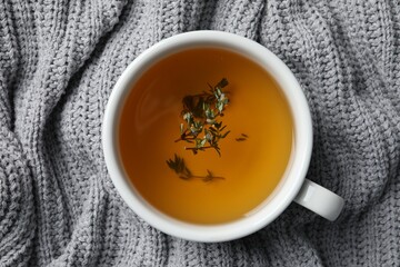 Cup of fresh thyme tea on light gray knitted blanket, top view