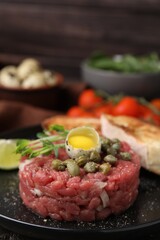 Tasty beef steak tartare served with quail egg and other accompaniments on black plate, closeup