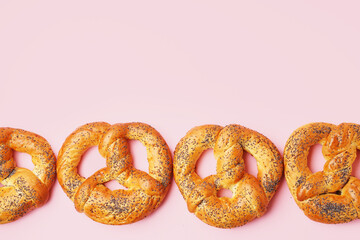 Delicious pretzels with poppy seeds on pink background
