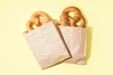 Paper bags with tasty pretzels on color background