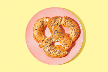 Plate with tasty pretzel on yellow background