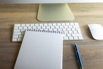 Notepad with pen on wooden table with computer and keyboard