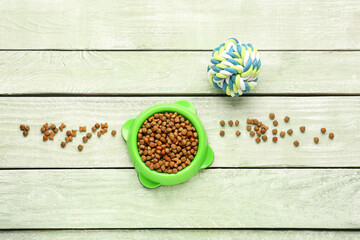 Fototapeta na wymiar Bowl of dry pet food and toy ball on color wooden background