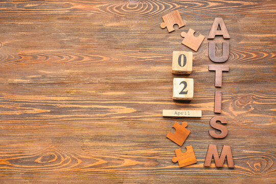 Word AUTISM with date 2 APRIL and puzzle pieces on wooden background