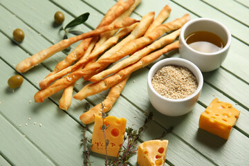 Tasty Italian Grissini with cheese, bowls of oil and sesame on green wooden background