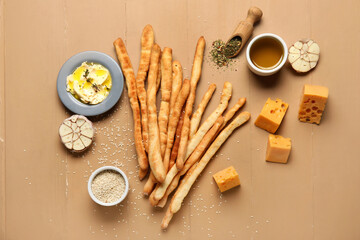 Composition with tasty Italian Grissini, cheese, butter, oil, sesame and garlic on beige wooden background