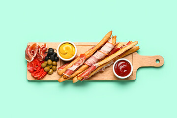 Wooden board of tasty Italian Grissini with bacon on turquoise background