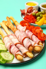 Plate of tasty Italian Grissini with bacon on turquoise background, closeup