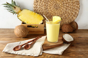 Fototapeta na wymiar Glass of tasty pineapple smoothie, straw and coconut on wooden table