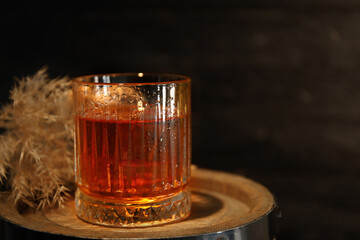 Glass of cold rum on barrel against wooden background