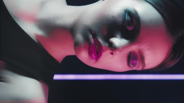Vertical video. Retro fashion. 90s girl. Night beauty look. red Purple blue color neon flash light relaxed teen model face with artistic makeup closed eyes posing on dark.